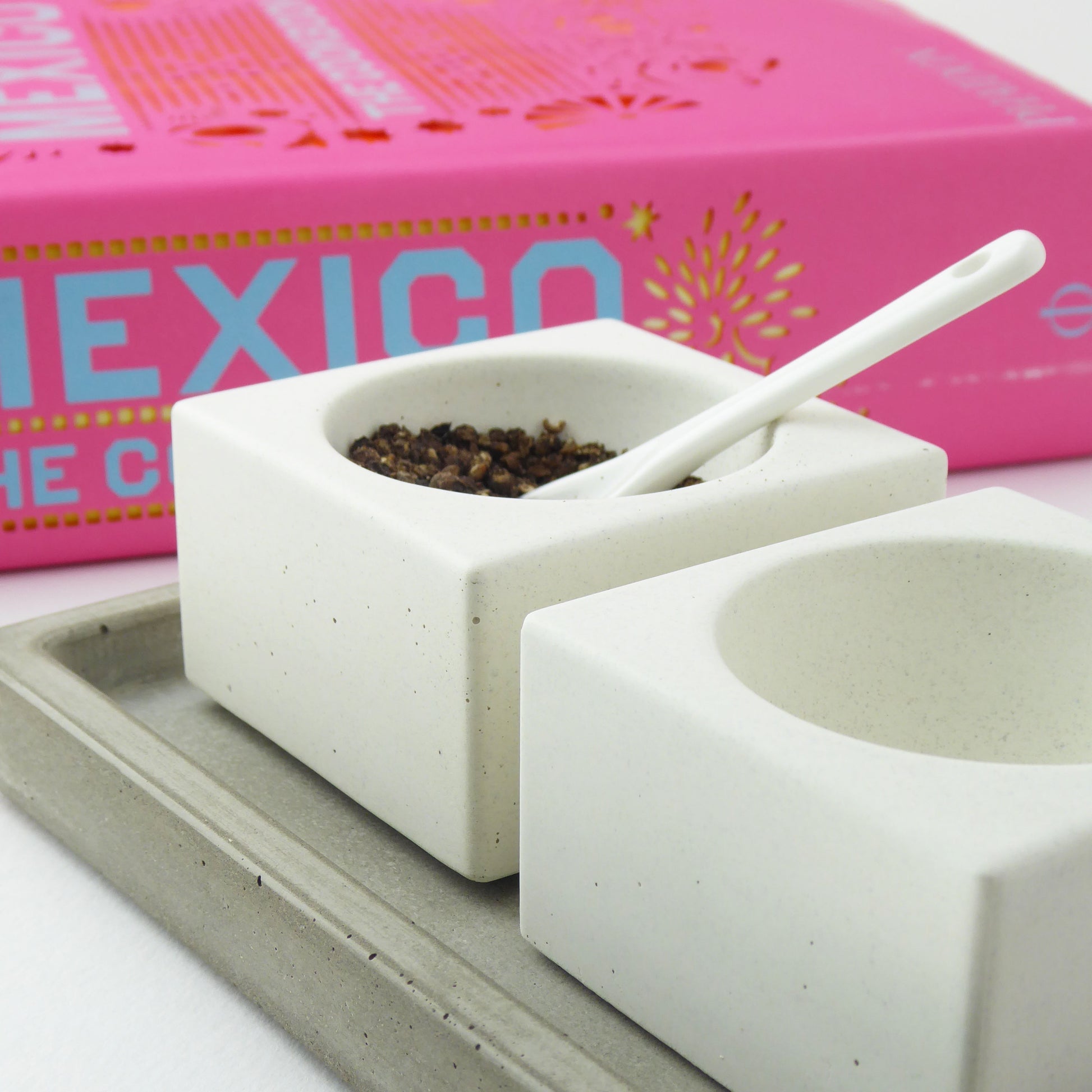 Pair of white ceramic salt and pepper bowls with a pink cookbook in the background