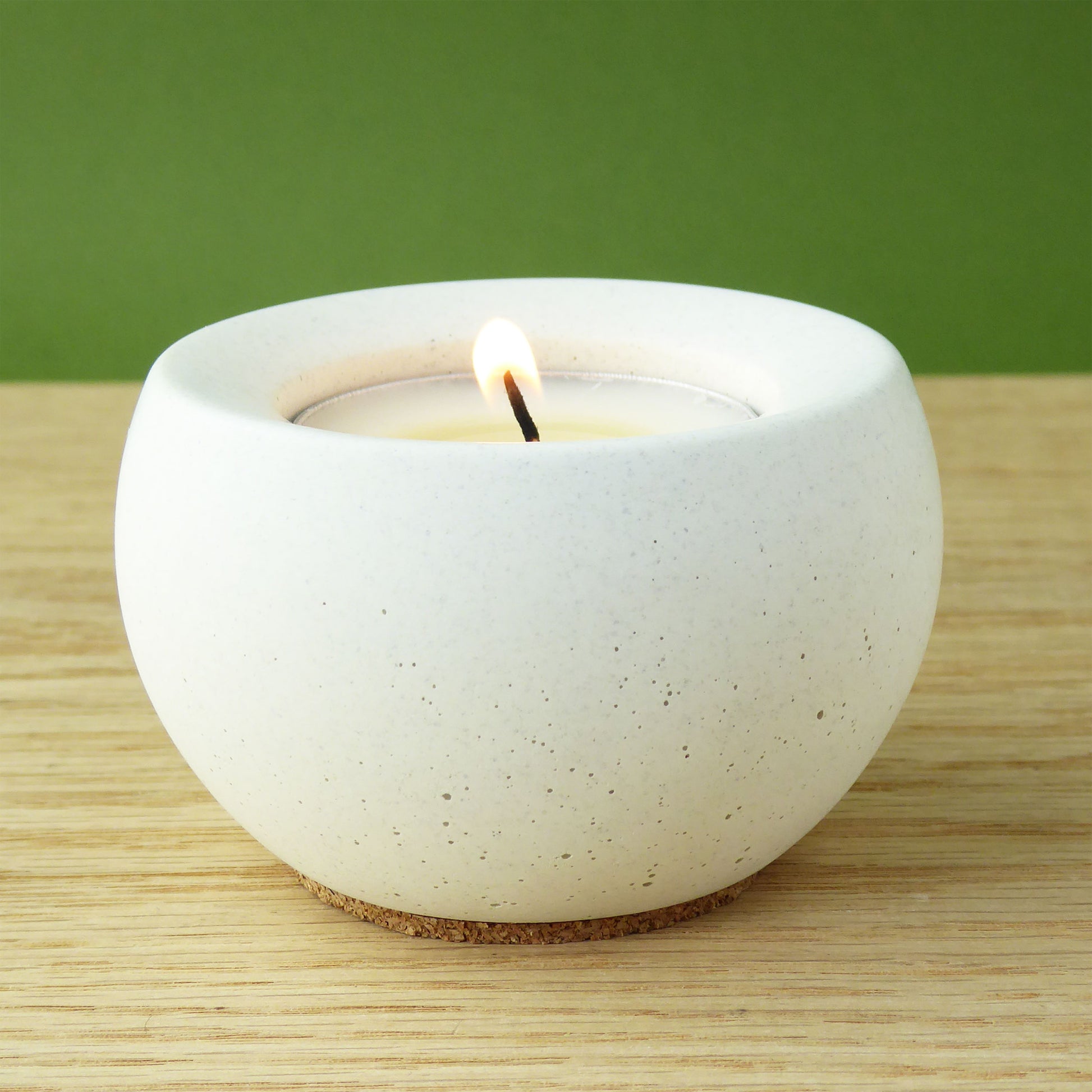 White concrete candle holder with a lit tea light on a wooden shelf