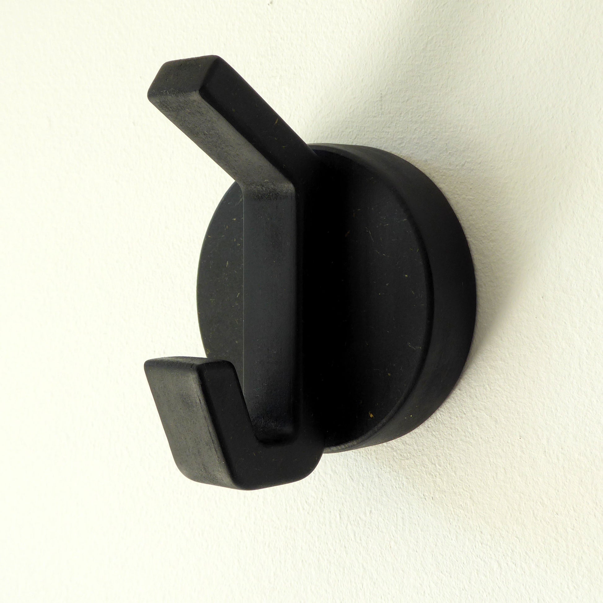 Minimalist black wooden wall hook mounted on a white wall