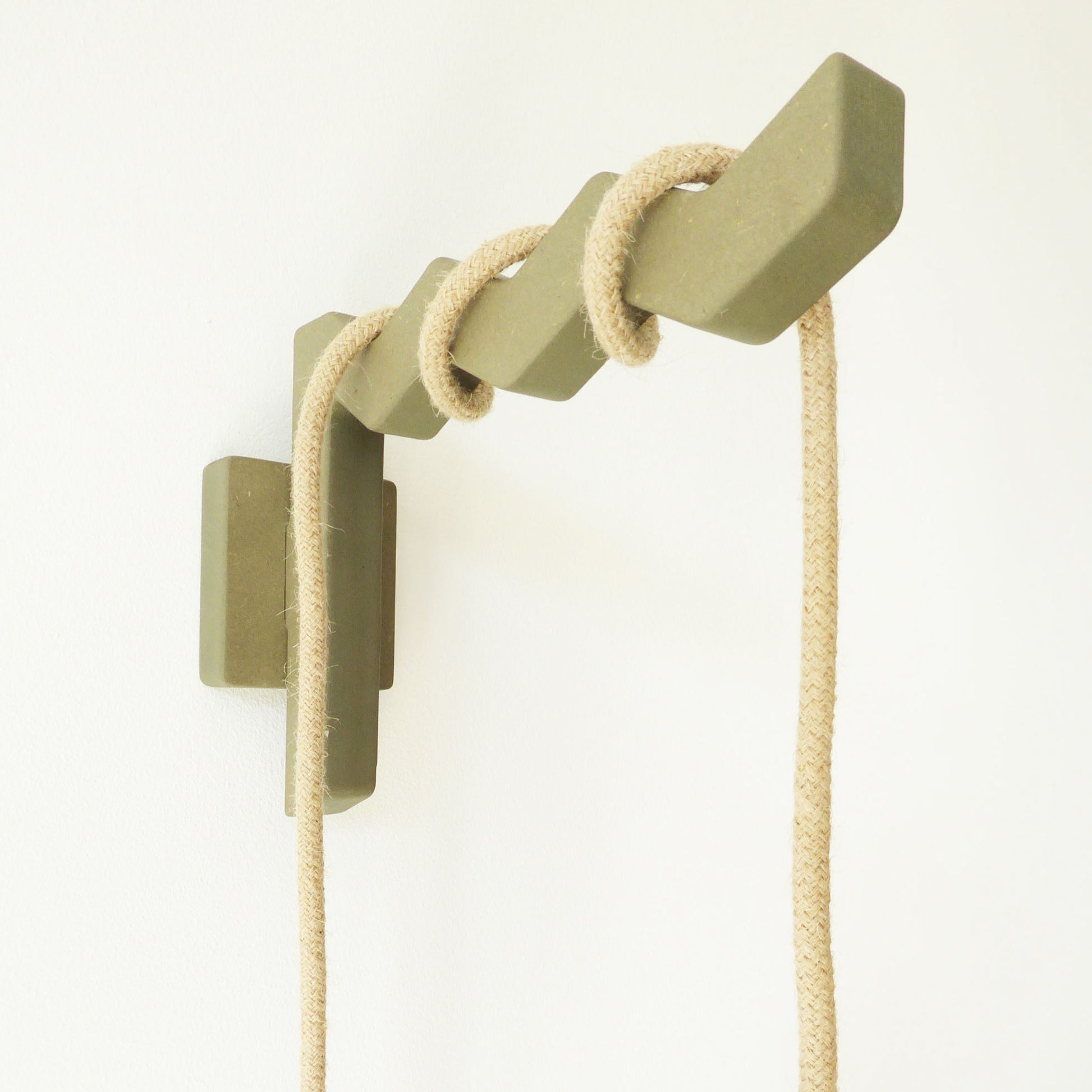 Wall mounted bracket with a zig zag design in a neutral sage coloured wood with a jute coloured cable wrapped around the arm