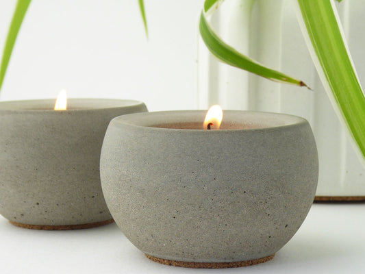 Pair of modern grey concrete candle holders with lit tea lights next to a plant pot 