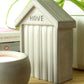 Small concrete beach hut-shaped ornament with 'HOVE' embossed in the design styled on a wooden shelf with books and a houseplant in the background.
