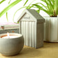 Concrete beach hut ornament embossed with the word 'HOVE' styled on a shelf next to books, a concrete tea light holder and a houseplant