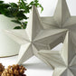 Geometric star-shaped scandi decorations on a white surface with a plant and pine cones in the background.