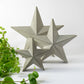 Three concrete star-shaped decorations on a white surface with a green plant.