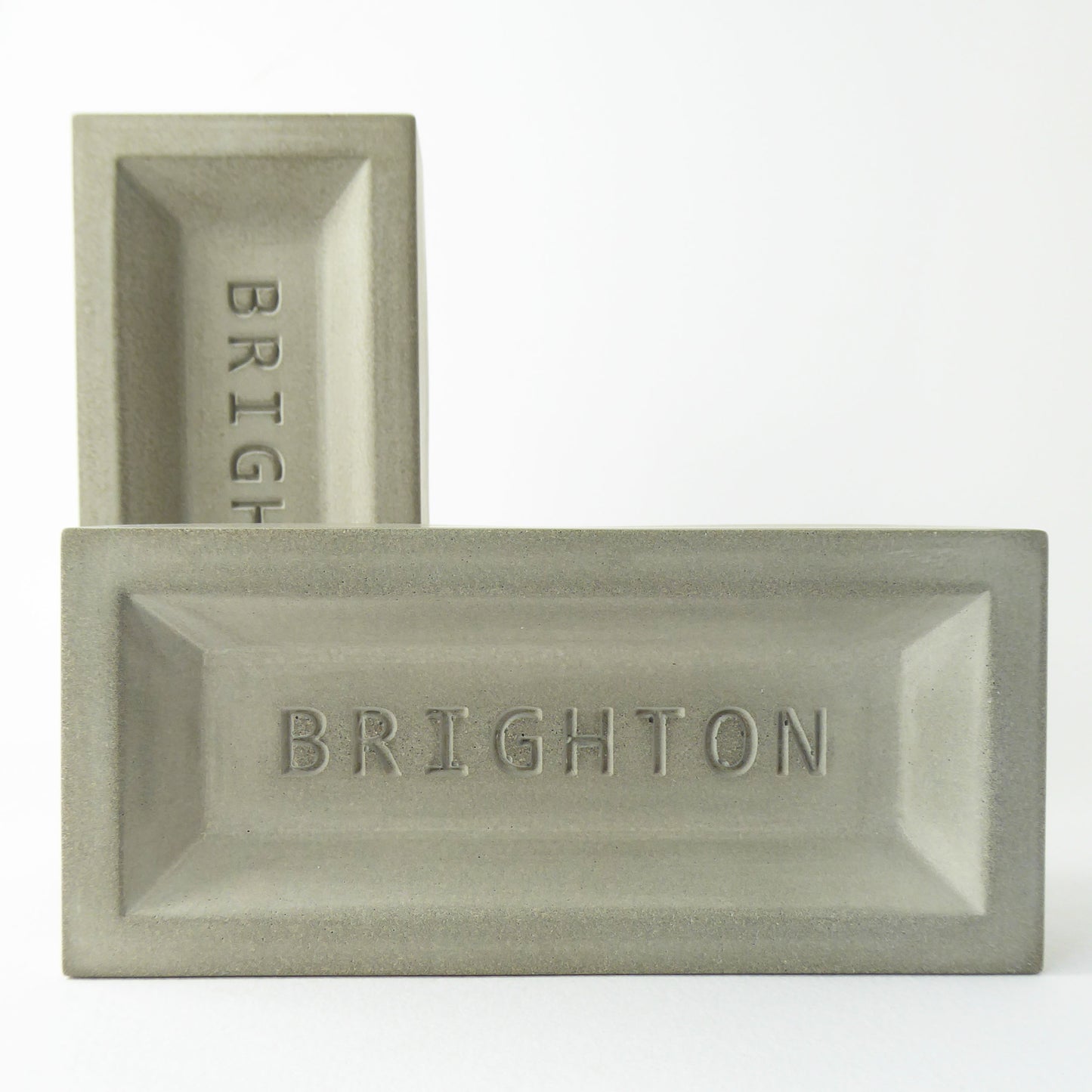 Two gray concrete brick objects with 'BRIGHTON' engraved on them