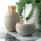 Raw grey concrete match pot holding long matches with a matching grey tea light candle holder positioned next to a succulent plant.