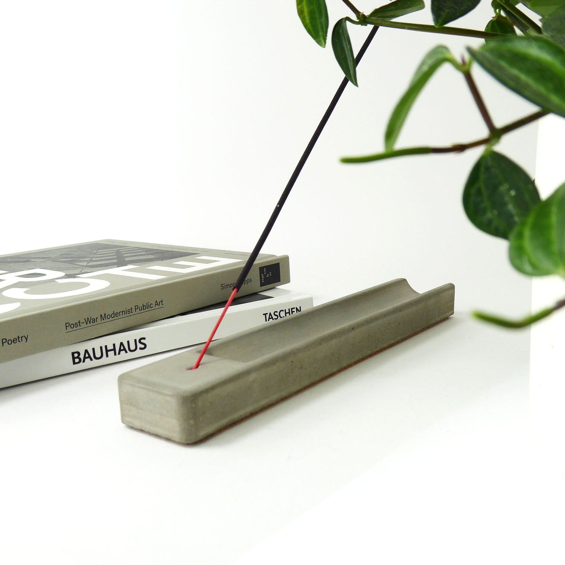 grey incense holder crafted from concrete styled next to some interior books and a houseplant