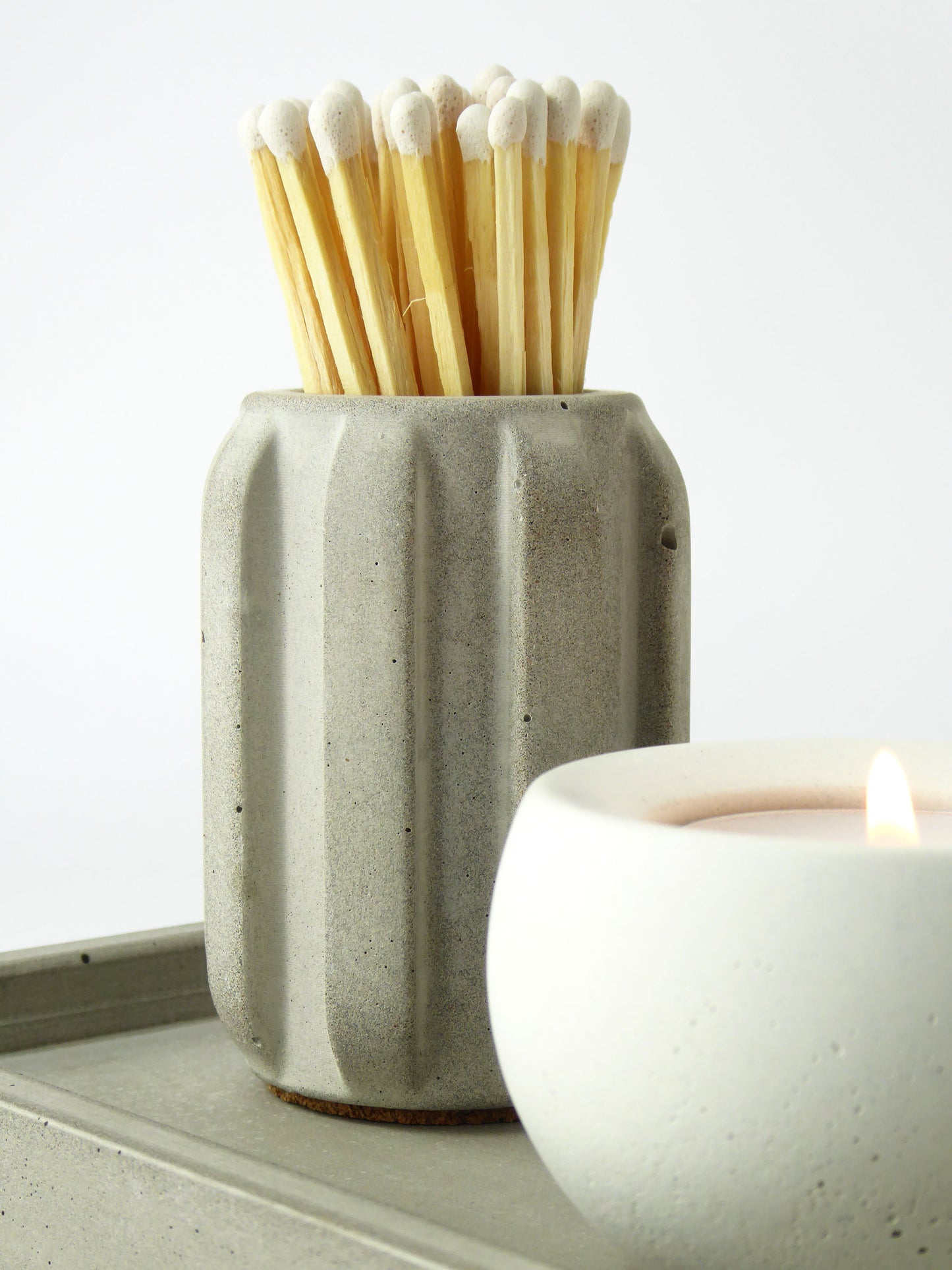 Concrete match holder with long matches next to a lit candle on a concrete tray