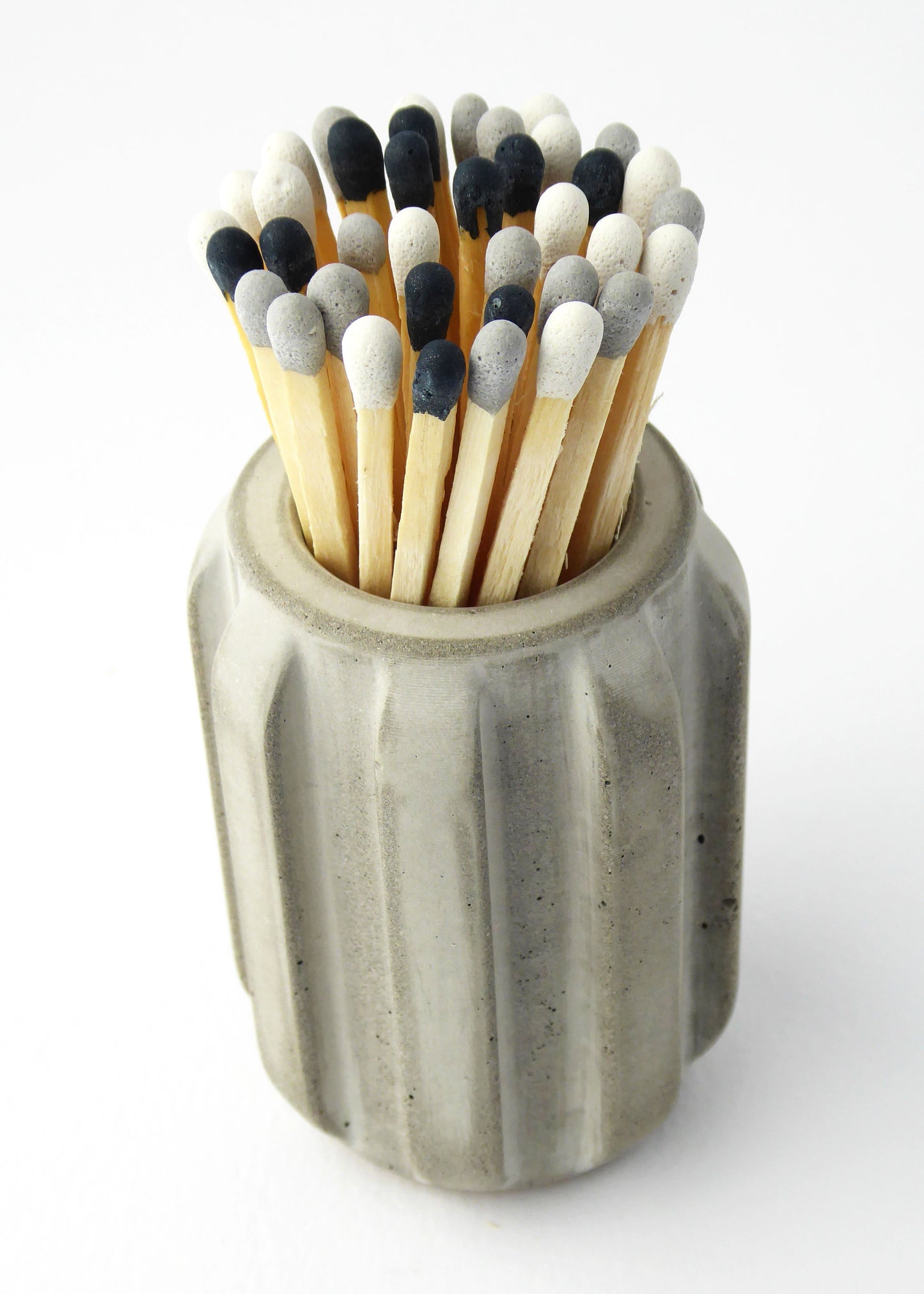 Long matches with black, white, and grey heads in a concrete pot holder with a ridged design on a white background