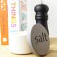 White concrete salt pot for storing salt flakes next to a pepper mill on a kitchen worktop next to some cookbooks