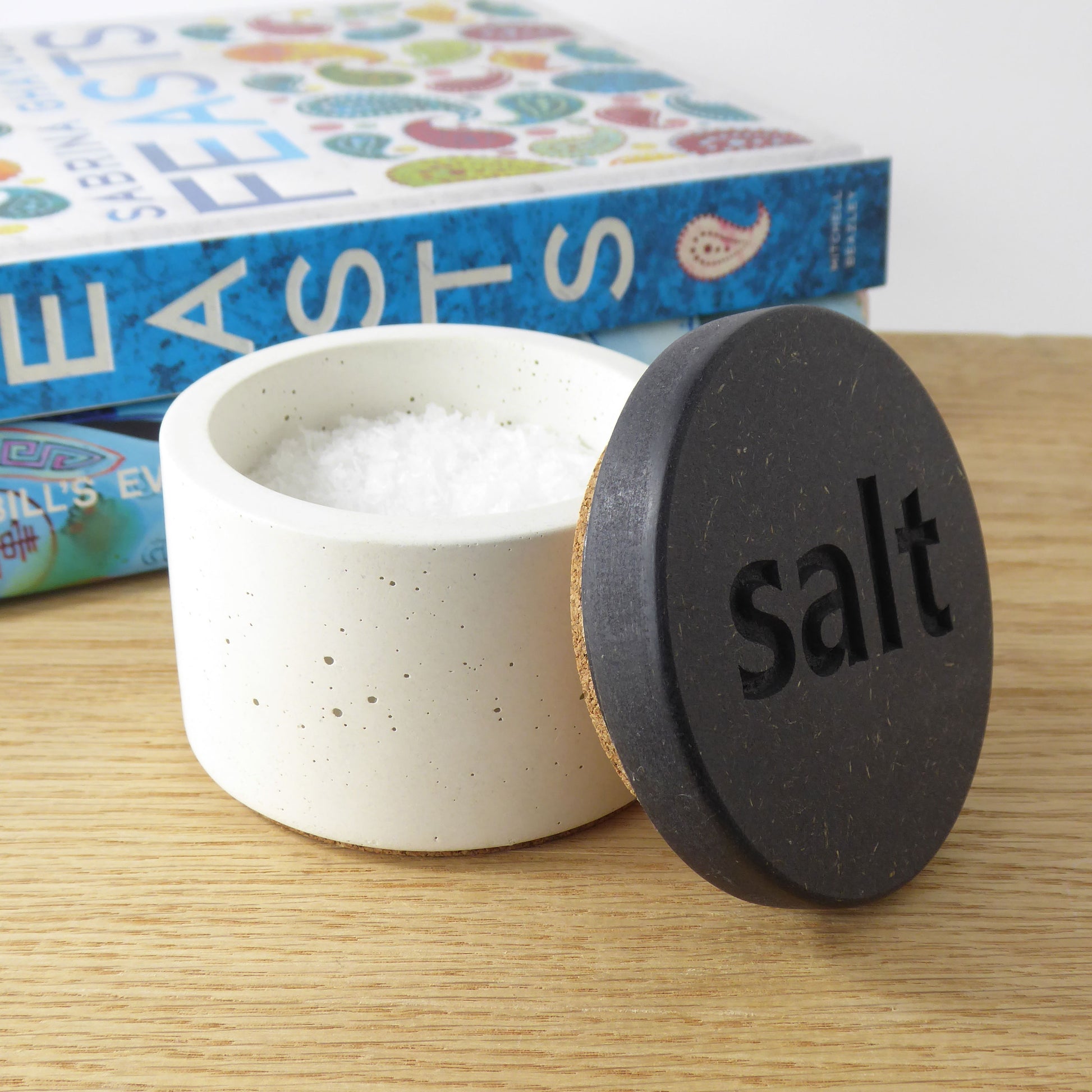 White concrete salt pot with a black wooden lid with the word 'salt' engraved on it. 