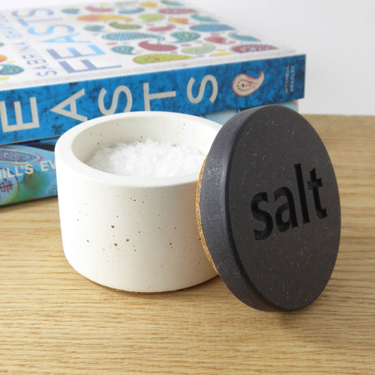 White concrete salt pot with a black wooden lid with the word 'salt' engraved on it. 
