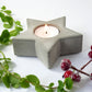 Star-shaped concrete candle holder with a lit candle, surrounded by greenery and Christmas berries on a white background