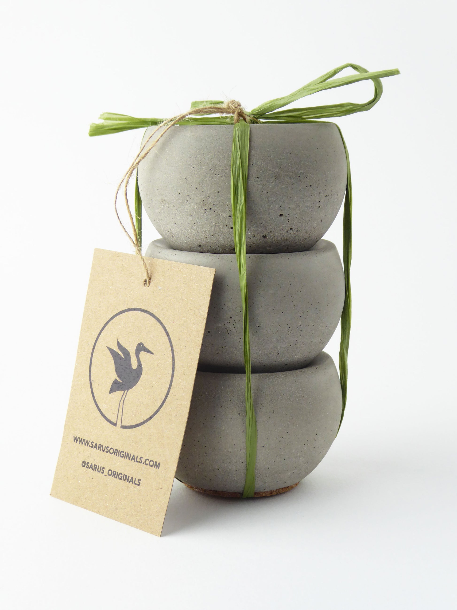 Stack of 3 concrete tea light holders tied with a green ribbon on a white background