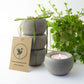 Set of 3 concrete candle holders with a lit candle, tied with green gift ribbon, on a white background.