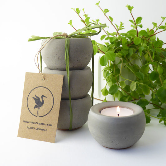 Set of 3 concrete candle holders with a lit candle, tied with green gift ribbon, on a white background.