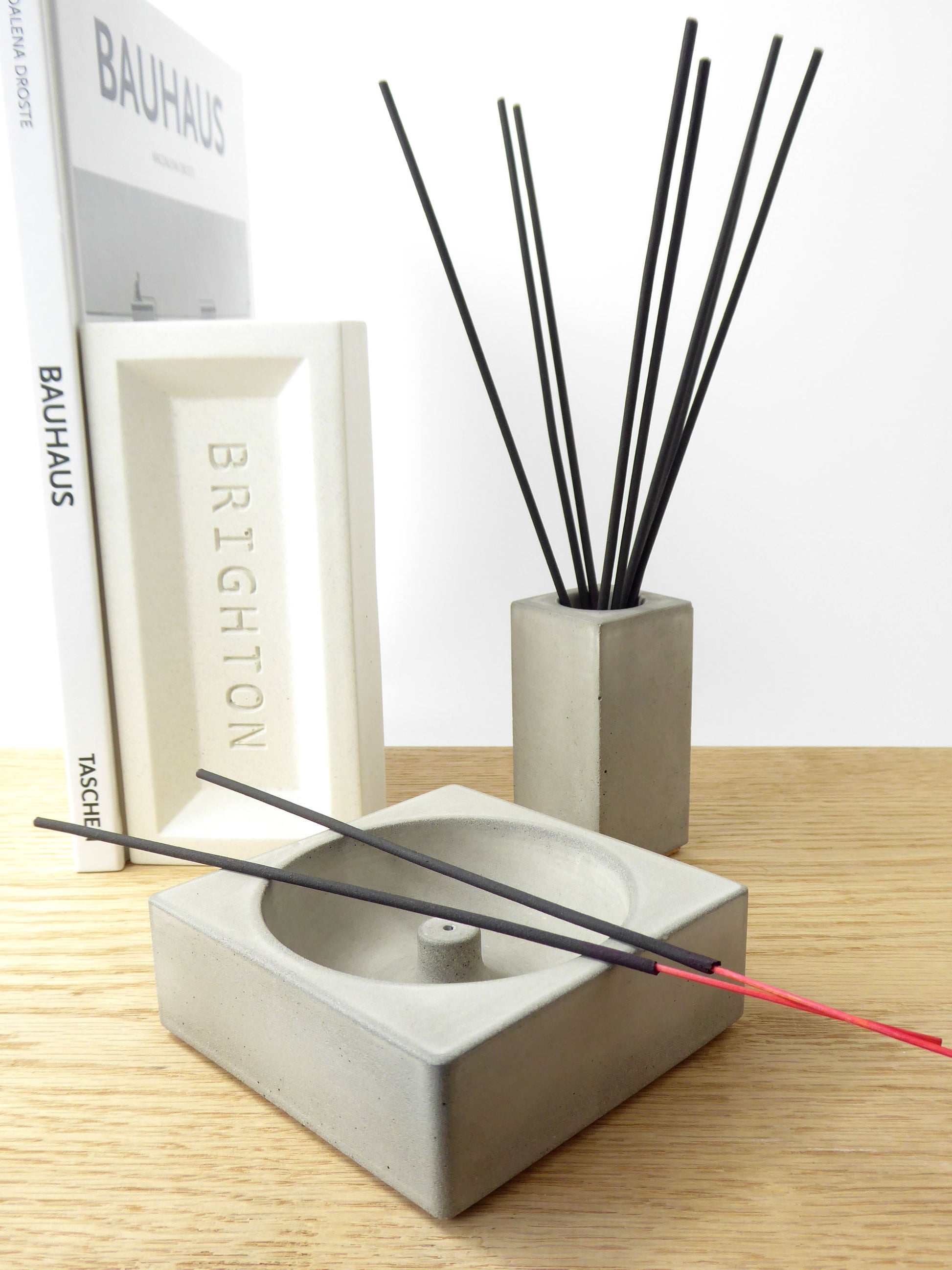 Concrete incense holder with black incense sticks on a shelf with a concrete pot holding incense sticks