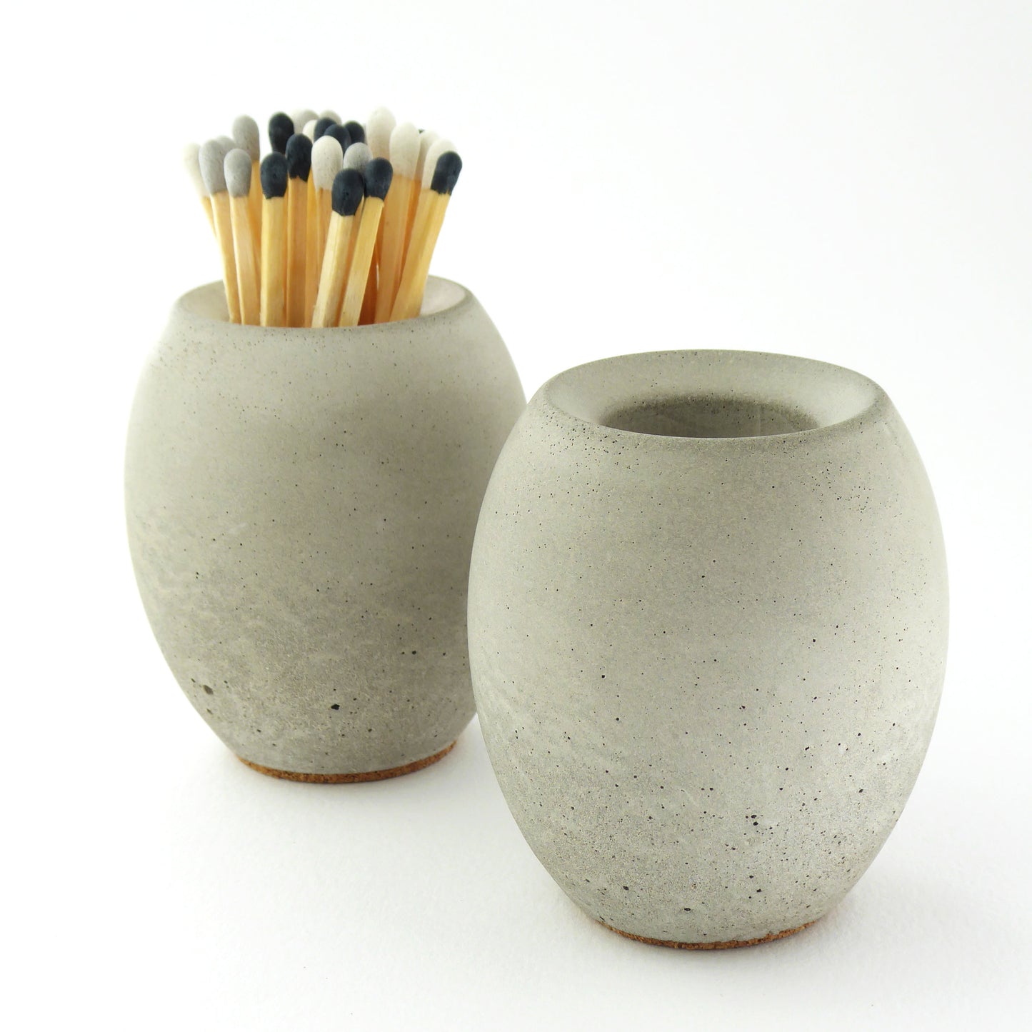 Two grey concrete match stick holders with long coloured matches on a white background