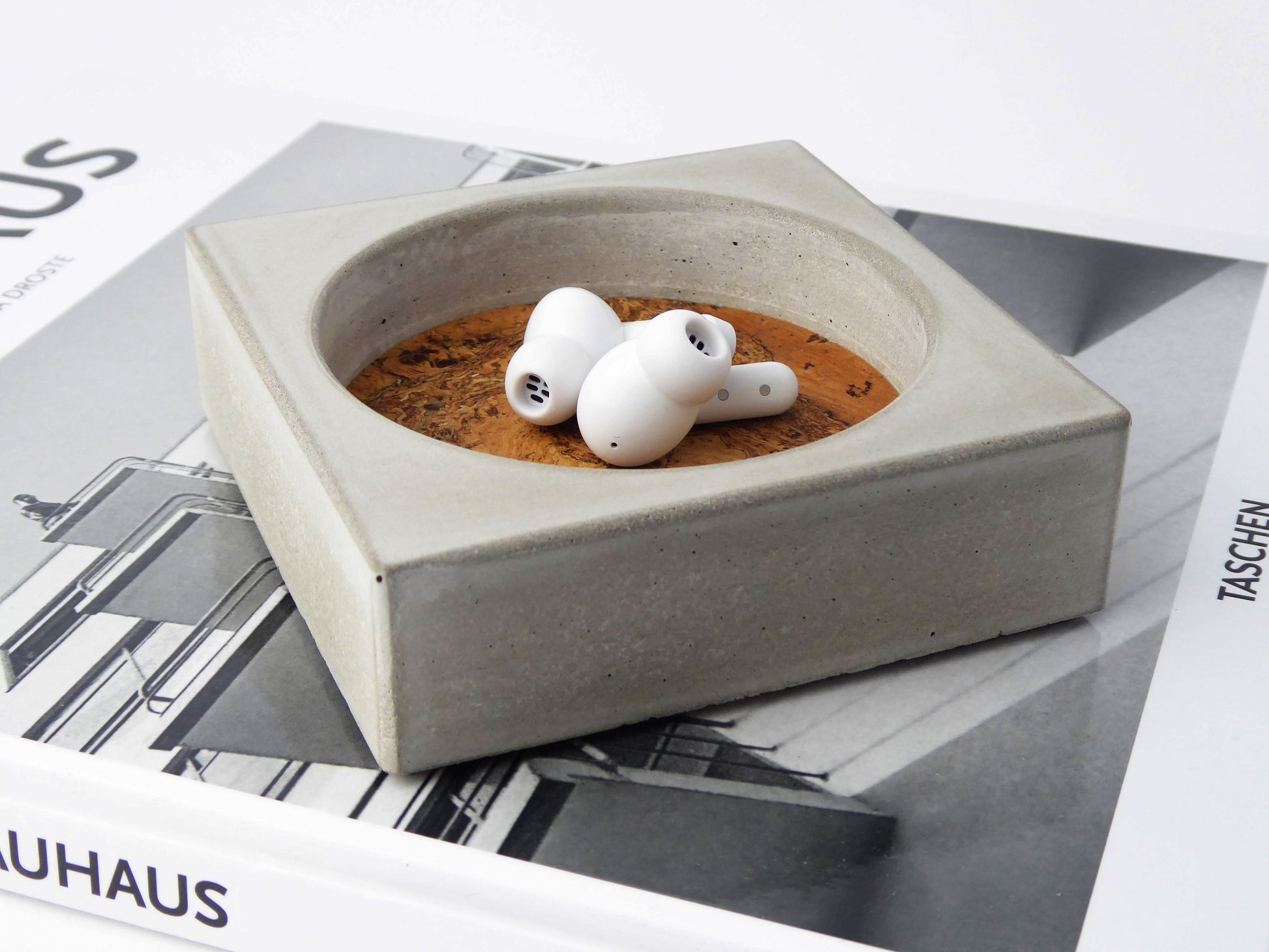 Grey concrete square trinket tray with a cork insert containing white ear buds
