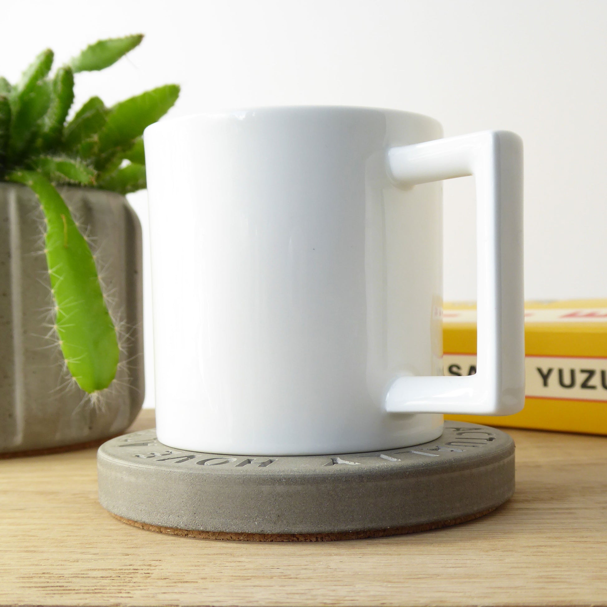 White mug on a concrete coaster with a house plant and books in the background