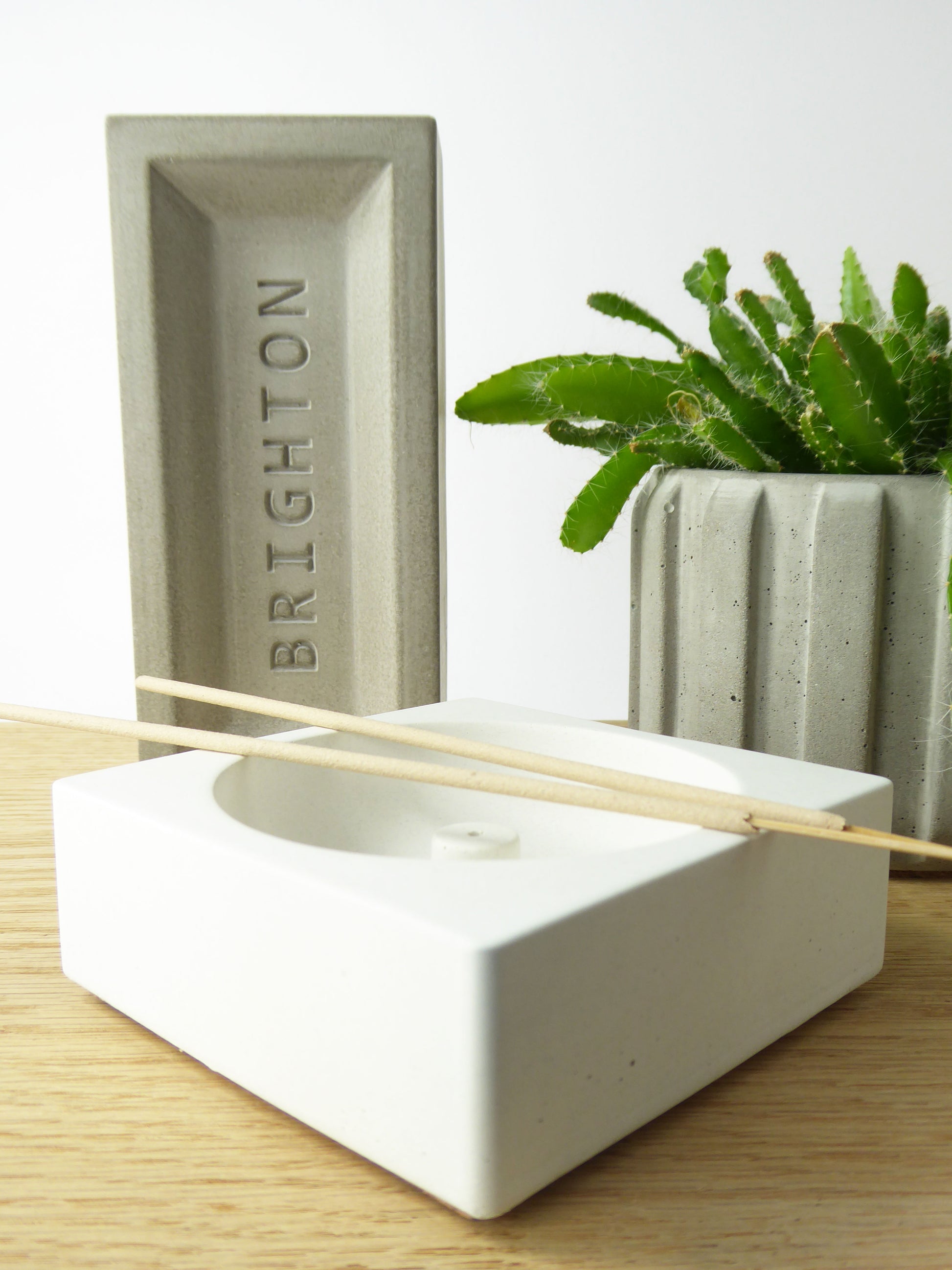 Concrete heritage brick with 'Brighton' embossed on it on a shelf next to an incense holder and a houseplant