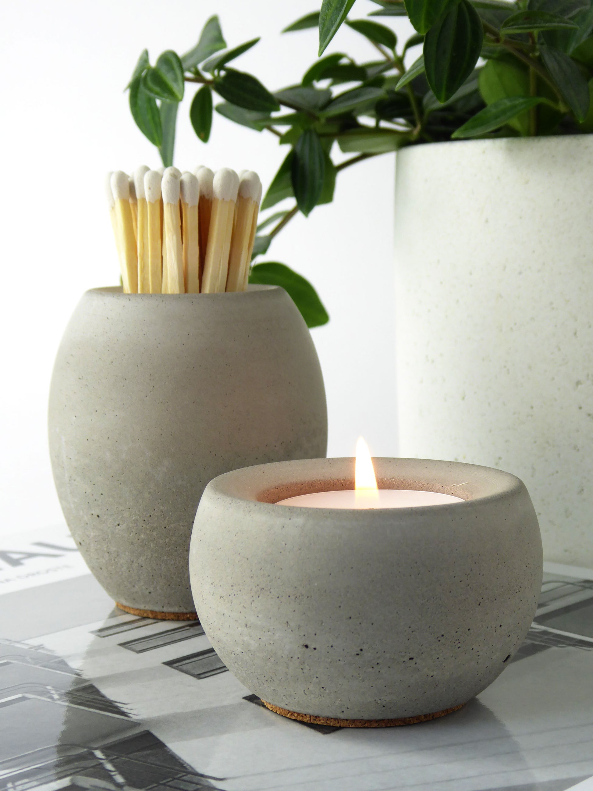 Grey concrete pot with long matches and alongside a matching concrete candle holder with lit candle