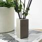 Concrete pot holding black incense  sticks next to a houseplant
