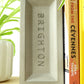 Concrete brick bookend with 'Brighton' engraved on it, propping up books on a shelf.