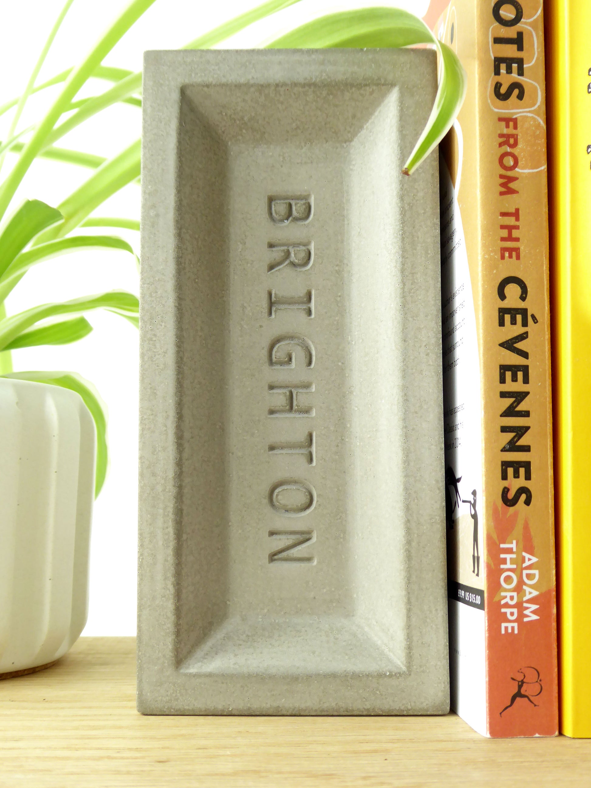 Concrete brick bookend with 'Brighton' engraved on it, propping up books on a shelf.