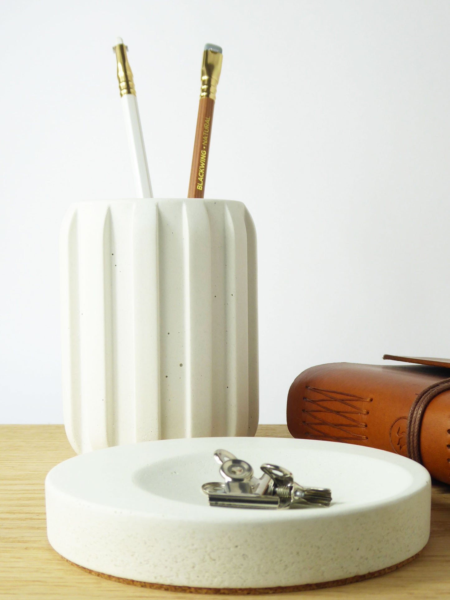 White concrete desk accessories and a leather notebook on a wooden desk
