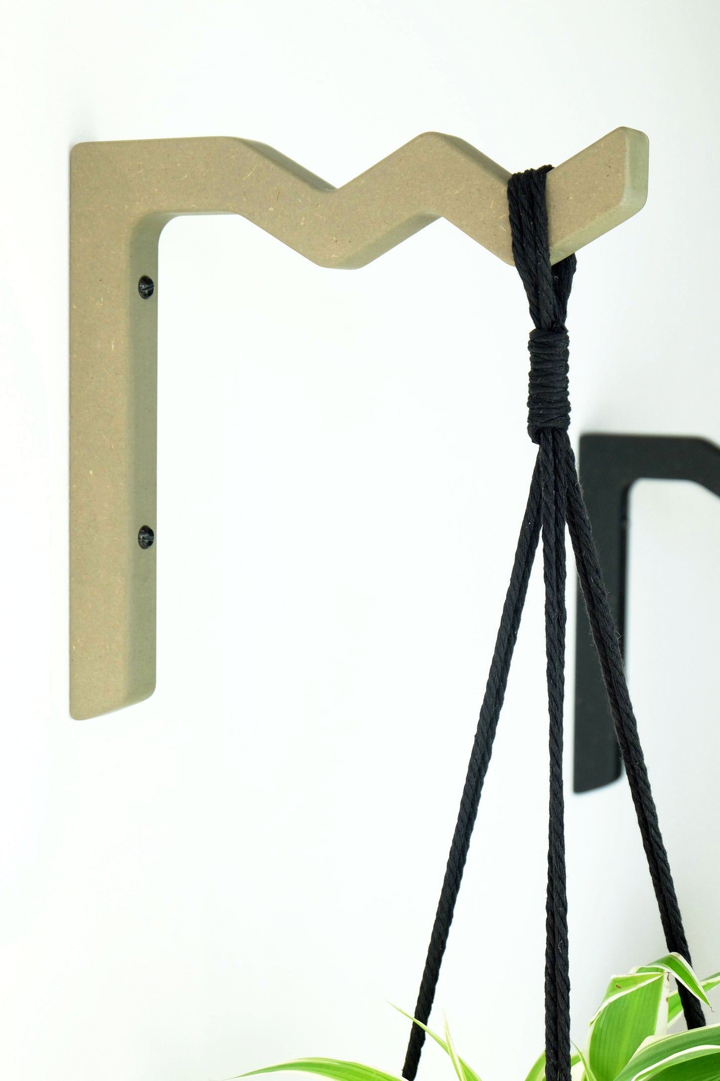 wall mounted plant bracket in a soft sage colour with a black macrame hanger hung from it
