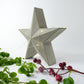Decorative free standing raw concrete star decoration with string lights on a white background with greenery and festive berries.