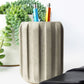 Concrete pencil holder with pens and a plant on a white surface next to a leather journal