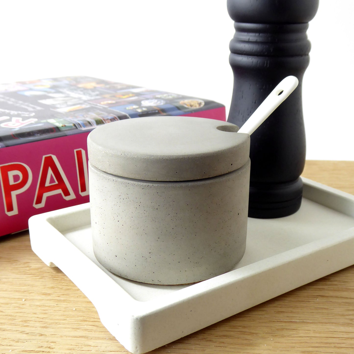 Grey concrete salt pot on a tray next to a black wooden pepper mill