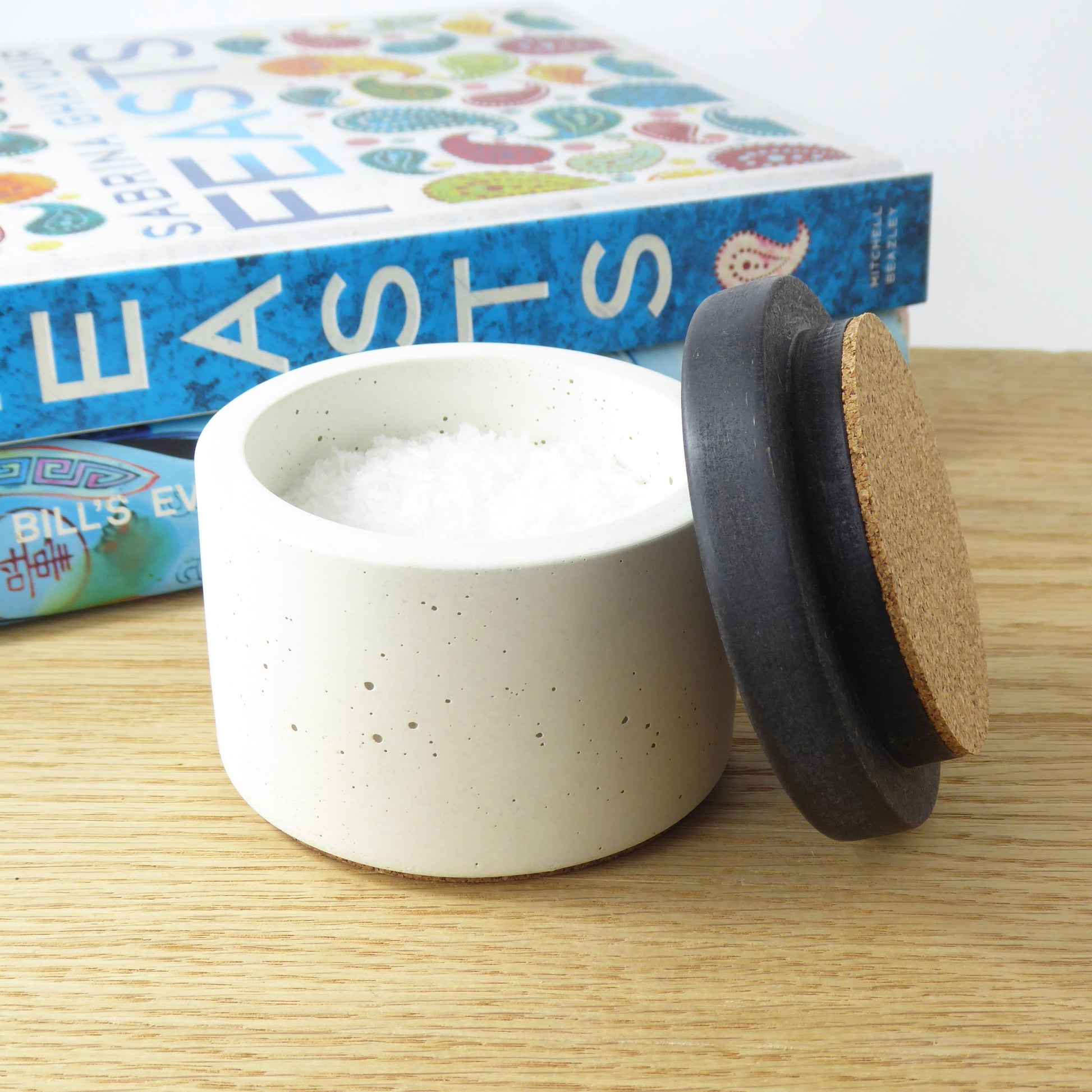White concrete container holding salt flakes with a black wooden lid lined with cork
