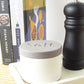 Salt pot container and pepper grinder on a shelf with cookbooks in the background
