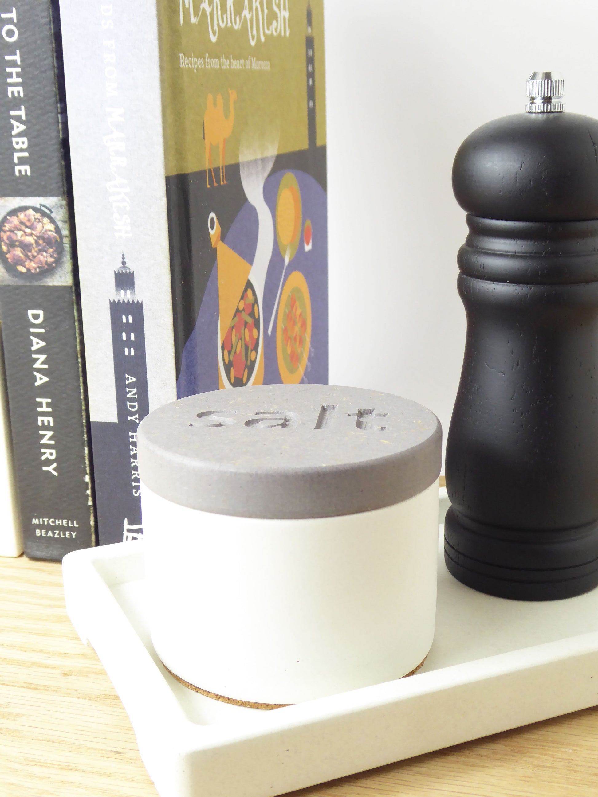 Salt pot container and pepper grinder on a shelf with cookbooks in the background