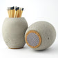 Grey concrete match holder with long matches and another match pot showing the base of the pot with its match striker pad