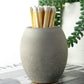 Grey concrete match stick holder with long 10cm matches on a table with plants in the background