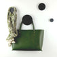 A set of black decorative wooden wall hooks of five different sizes displayed on a white wall, with one hook holding a green leather bag and another holding a multicoloured green scarf.