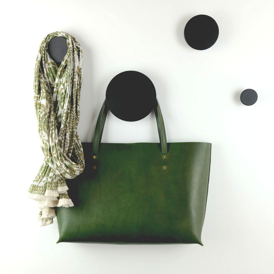 A set of black decorative wooden wall hooks of five different sizes displayed on a white wall, with one hook holding a green leather bag and another holding a multicoloured green scarf.