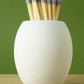 White concrete match pot with long matches with grey coloured tips on a wooden surface and green background