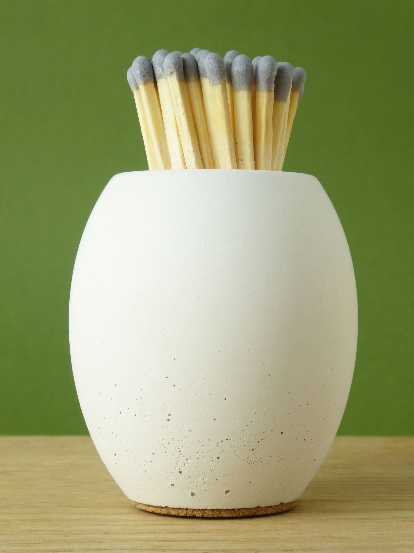 White concrete match pot with long matches with grey coloured tips on a wooden surface and green background