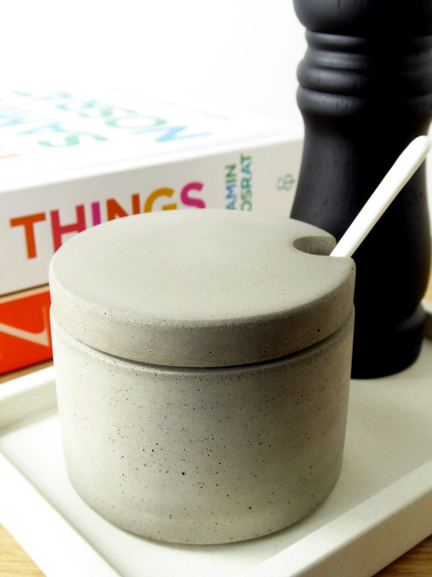 Grey concrete salt pot next to a black pepper grinder and some cook books
