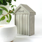 Small concrete beach hut shaped collectible with HOVE embossed in the design on the front next to a white concrete candle and houseplant