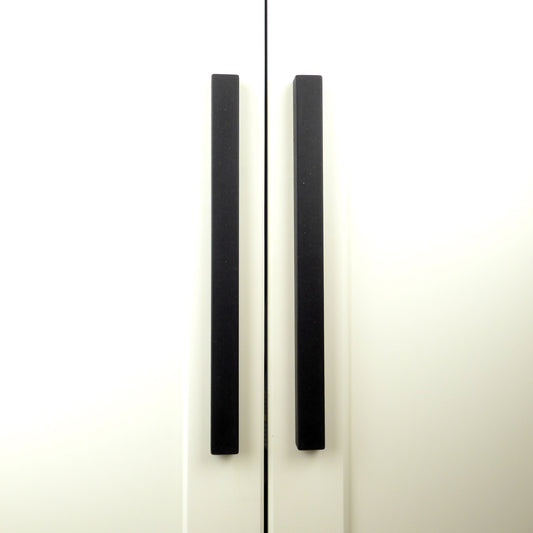 Pair of longline black cupboard door handles on a white kitchen unit