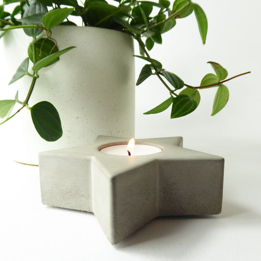 Concrete star-shaped candle holder with a lit candle and a green plant on a white background