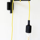 Wall-mounted light bracket with a yellow plug-in pendant cord wrapped around the arm on a white wall