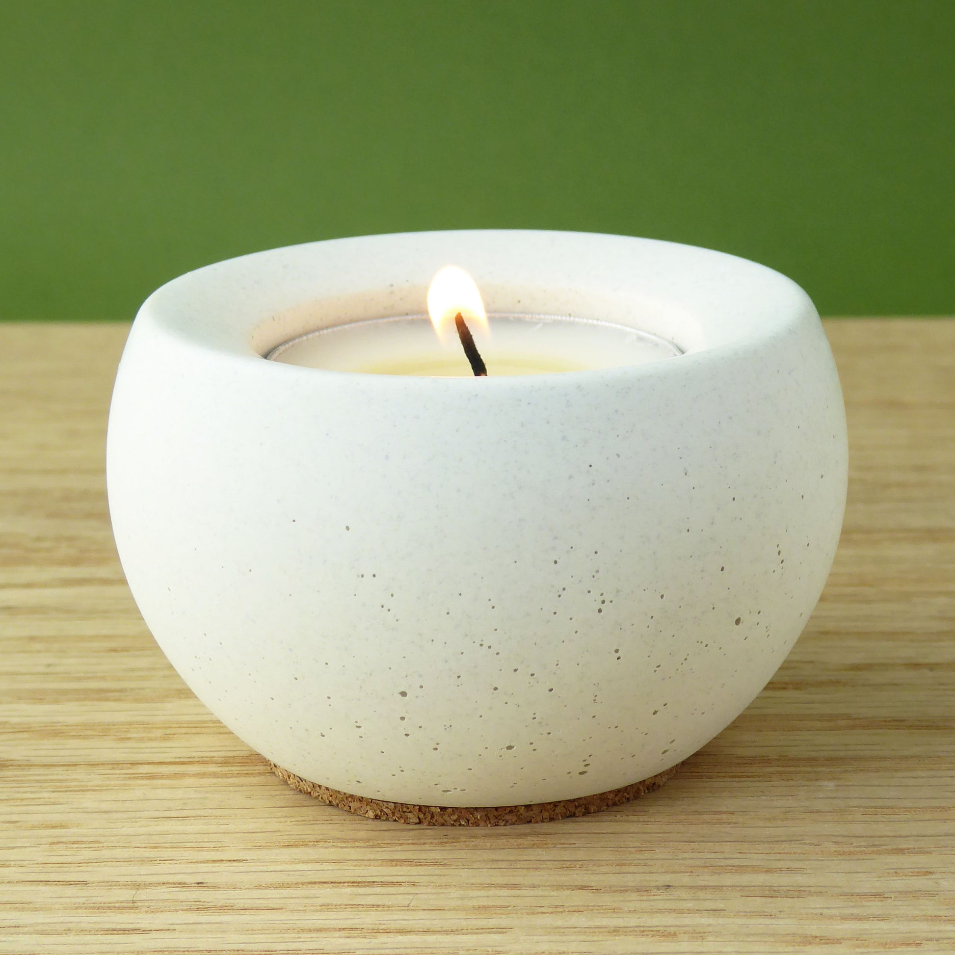 White ceramic candle holder with a lit candle on a wooden surface and green background